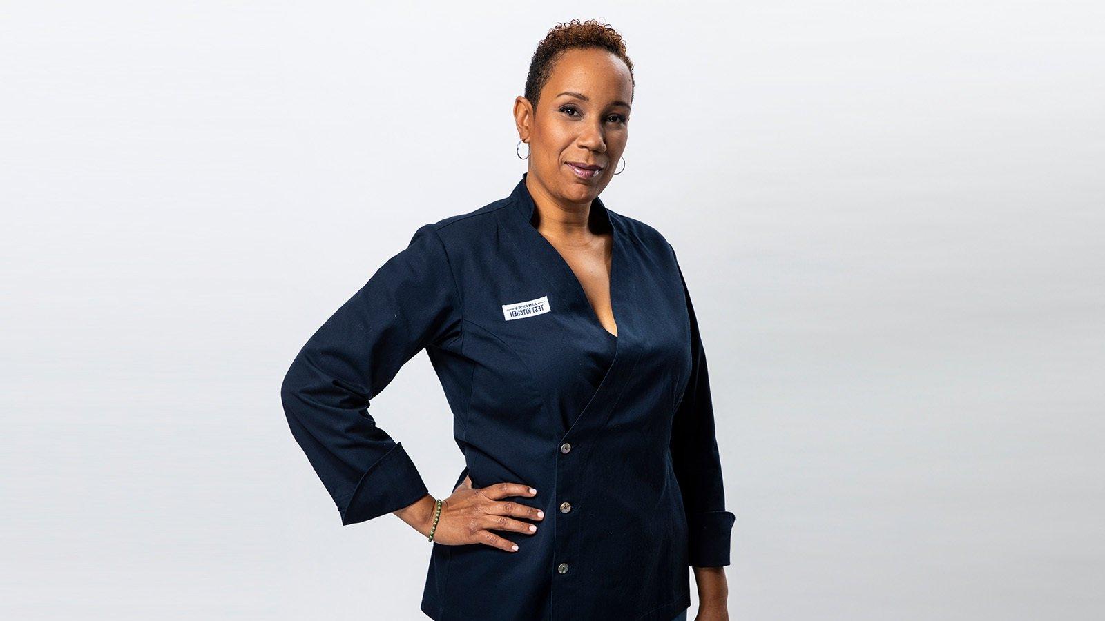 Grad Elle Simone Scott standing and smiling against a white backdrop while wearing a blue double-breasted chef's jacket with an America's Test Kitchen patch on the breast.