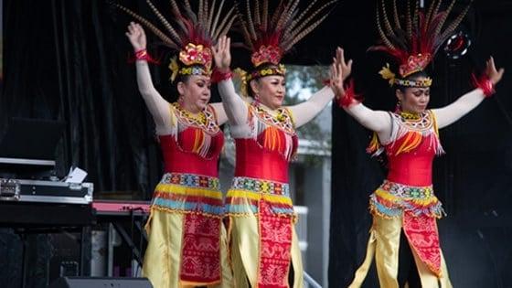 Three women dancing in colorful Indonesian feathered headdresses, 黄色的裙子, 还有串珠腰带和衣领.