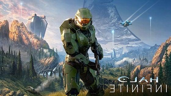 Halo main character Master Chief in signature green armor featuring the number 117 on his left chest plate in white, centered in front of a large grey triangular space ship with the words ‘Halo Infinite’ stylized in the bottom left corner.