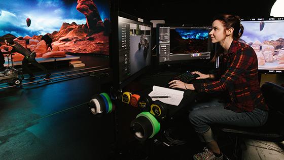 一个女人坐在桌子前，面前是几台显示器. She is in a virtual production studio that has been designed to look similar to Mars.