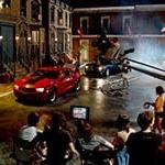 Full Sail University's Backlot in the evening filled with a full film production crew shooting a scene featuring two muscle cars, one red and one black.
