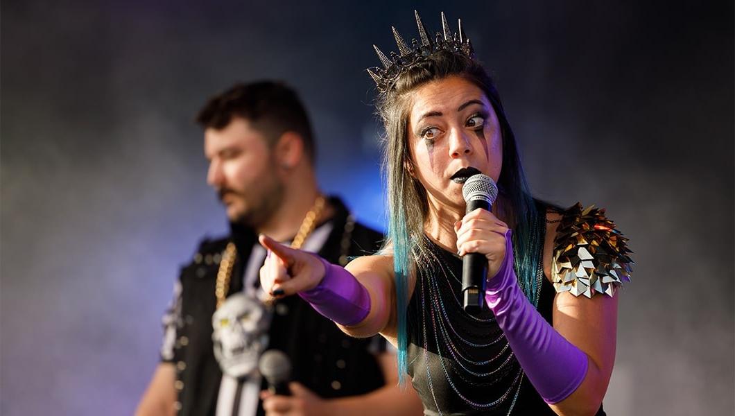 一个戴着金属王冠、化着舞台妆的女人指着外面，对着人群做着夸张的鬼脸.